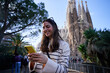 © Gigi Delgado - Cheerful young woman using mobile phone in front of the sagrada familia basilica, enjoying her travel experience connected to internet. Copy space.