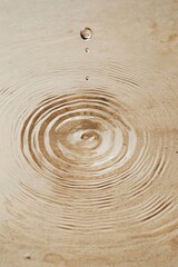 Poster - Soft ripples form gracefully on a beige surface as a single droplet descends, capturing the tranquil essence of the moment. This serene display reflects calmness and simplicity