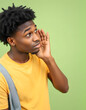 © Lola - Young curious nosy man of African American ethnicity he wearing yellow t-shirt casual clothes try to hear you overhear listening intently isolated on plain pastel green background. Lifestyle concept
