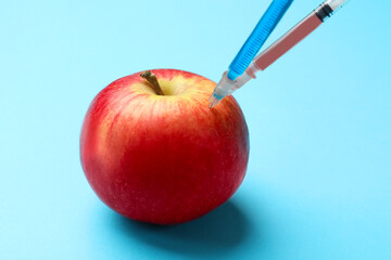 Wall Mural - GMO concept. Red apple with different syringes on light blue background, closeup