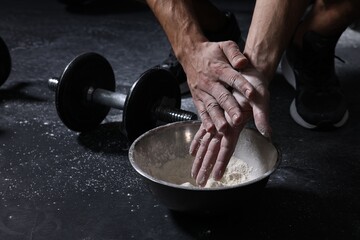 Wall Mural - Man applying talcum powder onto his hands above bowl before training in gym, closeup