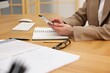 © New Africa - Secretary using smartphone at wooden table in office, closeup