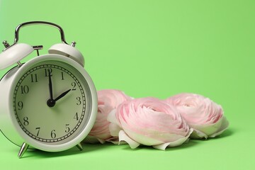 Poster - Spring time. Alarm clock and beautiful ranunculus flowers on green background, closeup