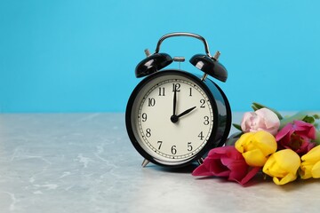 Poster - Spring time. Alarm clock and beautiful tulips on grey marble table against light blue background, space for text
