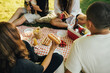 © polinaloves - Happy people having picnic with hot dogs and cold drinks, sitting on a plaid in a park.