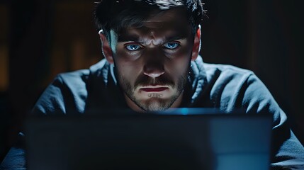 Poster - Young Caucasian man with intense blue eyes illuminated by laptop screen in dark room, dramatic lighting creates mysterious atmosphere for cybersecurity and hacking concepts.