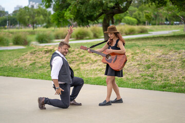 Man dances flamenco while female guitarist plays guitar in a park