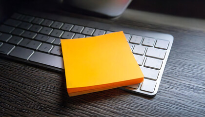 Modern workspace close-up: a bright yellow sticky note rests on a sleek silver keyboard, atop a dark wood desk.  Perfect for concepts of productivity, reminders, ideas, and modern office life.