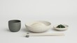 © danadesa - Minimalist Japanese table setting featuring a bowl of udon noodles, a ceramic cup, and chopsticks on a clean white background.