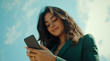 © Enrique - a smart beautiful young hispanic businesswoman in side profile, turned towards the left, happy, looking at her phone, looking down into the phone. wearing forest green formals , aspirational