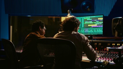 Fototapete - Diverse team of artist and sound designer working on editing tunes for a new hit, operating mixing console with moving faders and colored meters. Musician and producer making tracks. Camera B.