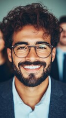 Portrait of a smiling young man with glasses. He has dark curly hair and a beard. Close-up shot.