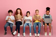 © Prostock-studio - E-learning concept. Focused diverse schoolkids with gadgets and study materials sitting on chairs against pink background