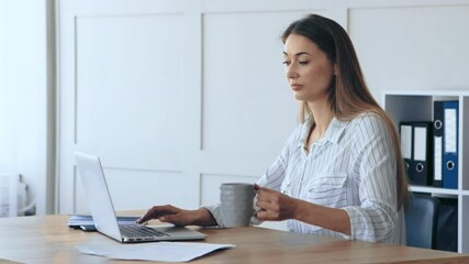 Poster - A woman sits at a wooden desk, focused on her laptop while holding a mug of coffee. The office is well-lit, featuring organized folders and a calm atmosphere conducive to productivity.