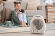 © Pixel-Shot - Electric fan heater on floor against little girl playing video game at home, closeup