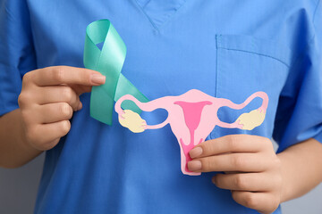 Wall Mural - Female doctor holding turquoise ribbon with paper uterus, closeup. Cervical Health Awareness Month