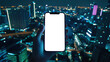 © chekart - Nightlife. Close-up of a young woman holding a cell phone with an empty white screen against a night-time urban landscape with burning lights. A phone mockup to advertise a mobile app
