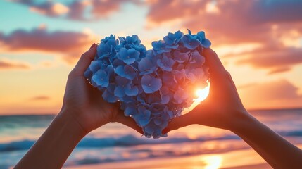 Poster - A woman hands carefully shape blue hydrangea flowers into a heart at sunset on a beach, creating a beautiful contrast with the colorful sky.