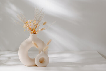 Fototapete - Bohemian calming still life composition with ceramic vase set and dry flower bouquet with sunlight shadows on the white table, copy space. Scandinavian home interior decoration
