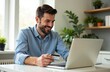 © Наталья Занкина - A happy man is sitting at a table with a laptop and a child's bank card in his hands, paying for an online purchase. Pocket money, financial literacy