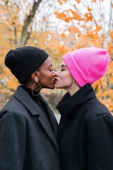 Sticker - Two women kissing each other while wearing black and pink hats. Scene is playful and lighthearted