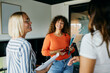 © Flamingo Images - Friendly Office Interaction Among Diverse Women in a Modern Workspace. The three women are talking together, smiling, with notebooks in their arms