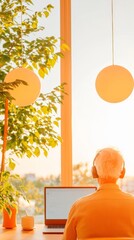 Fototapete - Biophilic Office Design Elderly Man Engaged in Remote Work with Laptop and Headphones in Sunlit, Green Workspace - Boosting Productivity in Modern Digital Workplaces