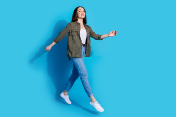 Wall Mural - Cheerful young woman walking joyfully against a blue background, showcasing trendy casual fashion and a lively demeanor