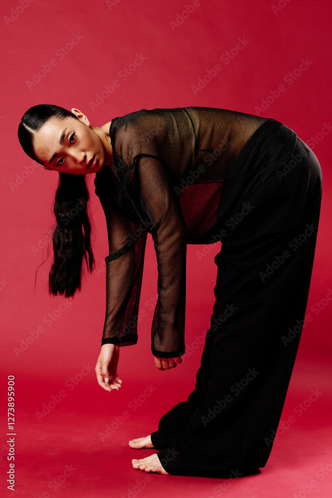 Asian woman in black pants and sheer top bending over on a red ...