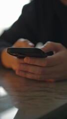 The man clicks the phone. in your hands while sitting at the table.
A man holds a smartphone in his hands and clicks something on the background.
A man uses his phone to make online purchases.
Online 