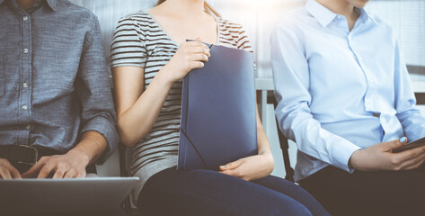 Wall Mural - Group of casual dressed business people sitting in a line while waiting for a job interview in sunny office