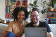 © Markus Schröder - Portrait of a smiling mixed race couple in their 30s watching computer laptop on the sofa at home