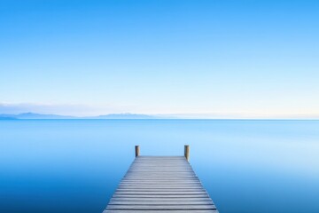  Wooden dock extends into calm, blue waters under a clear sky, mountains visible on the horizon