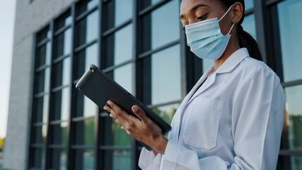 Poster - Medical professional wearing white lab coat and surgical mask browsing digital tablet near hospital window, representing modern healthcare technology and pandemic era communication