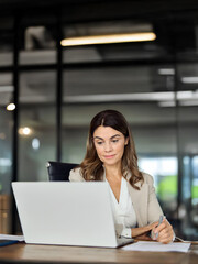 Wall Mural - Busy mid aged business woman working in office using laptop writing. 40 years old female professional executive manager looking at computer, elearning, having hybrid meeting at workplace.