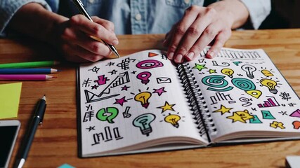 Aufkleber - Businesswoman draws colorful business ideas on a notebook, sitting at a wooden desk with colored pencils, pens, sticky notes, and a smartphone