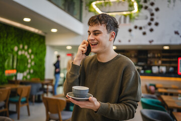 Wall Mural - young man student hold cup of coffee and talk on mobile phone at cafe