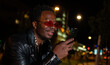 © liderina - African American man using mobile phone on the street in the night.