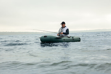 Wall Mural - Man fishing with rod from inflatable rubber boat on river