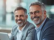 © Alexander Chaykin - Two smiling businessmen working together on laptops, sharing a positive and collaborative moment.