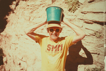 Man in Sunglasses Balancing a Green Bucket on His Head Outdoors