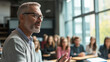 © Nick Freund - Engagierter Dozent mit Brille gestikuliert während einer Vorlesung. Helle, moderne Lernumgebung mit Studierenden im Hintergrund