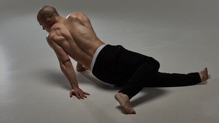 Rear view of shirtless male model moving on floor with sculpted back and elegant posture against minimalist backdrop. Concept of natural beauty, fashion and style, masculinity, confidence.