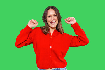 Joyful woman wearing a red sweater celebrates with raised arms against a green background