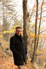 Caucasian man in autumn jacket and clothing posing on a forest trail, trees with autumn colors. The man is looking into the camera. Easy hiking trail in Brasov, Romania on Tampa mountain.