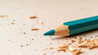 © Bonsales - Freshly sharpened turquoise pencil lies on a beige surface amidst wood shavings, evoking creativity and artistic endeavors