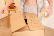 © ADDICTIVE STOCK - Young woman sealing a box labeled clothes with tape in moving day