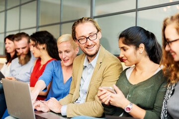 Aufkleber - Group of diverse people sitting together, using laptops and phones, smiling and interacting. Casual setting with a mix of men and women engaged in conversation. Diverse group of people photography.
