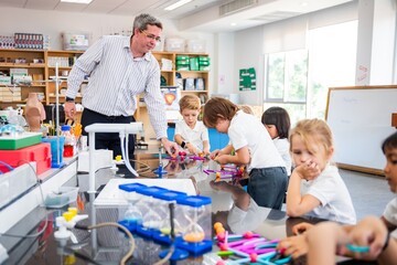Poster - Teacher guiding young students in a science classroom. Children engaged in hands-on activities. Educational setting with diverse students and teacher interaction. Science teacher teaching school kids.