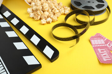 Wall Mural - Movie clapper, sweet popcorn, tickets and film reel on yellow background, closeup